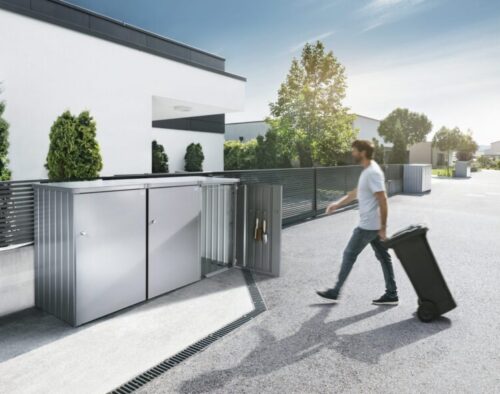 Mann mit Container vor drei verschiedenen Containerboxen vor einem grossen Haus.