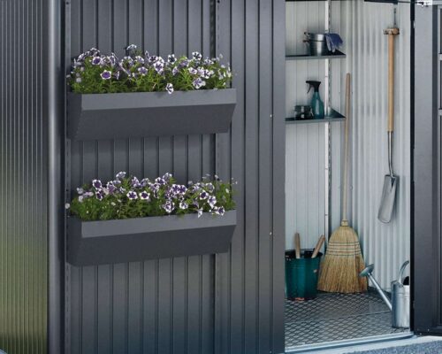 Biohort Floraboard in dunkelgrau an einem Gartenhaus in dunkelgrau angebracht. Die Türe rechts steht offen. Im Gartenhaus sind verschiedene Gartenutensilien verstaut.