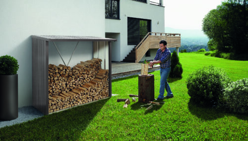 Man chopping wood in the garden in front of a dark gray firewood store