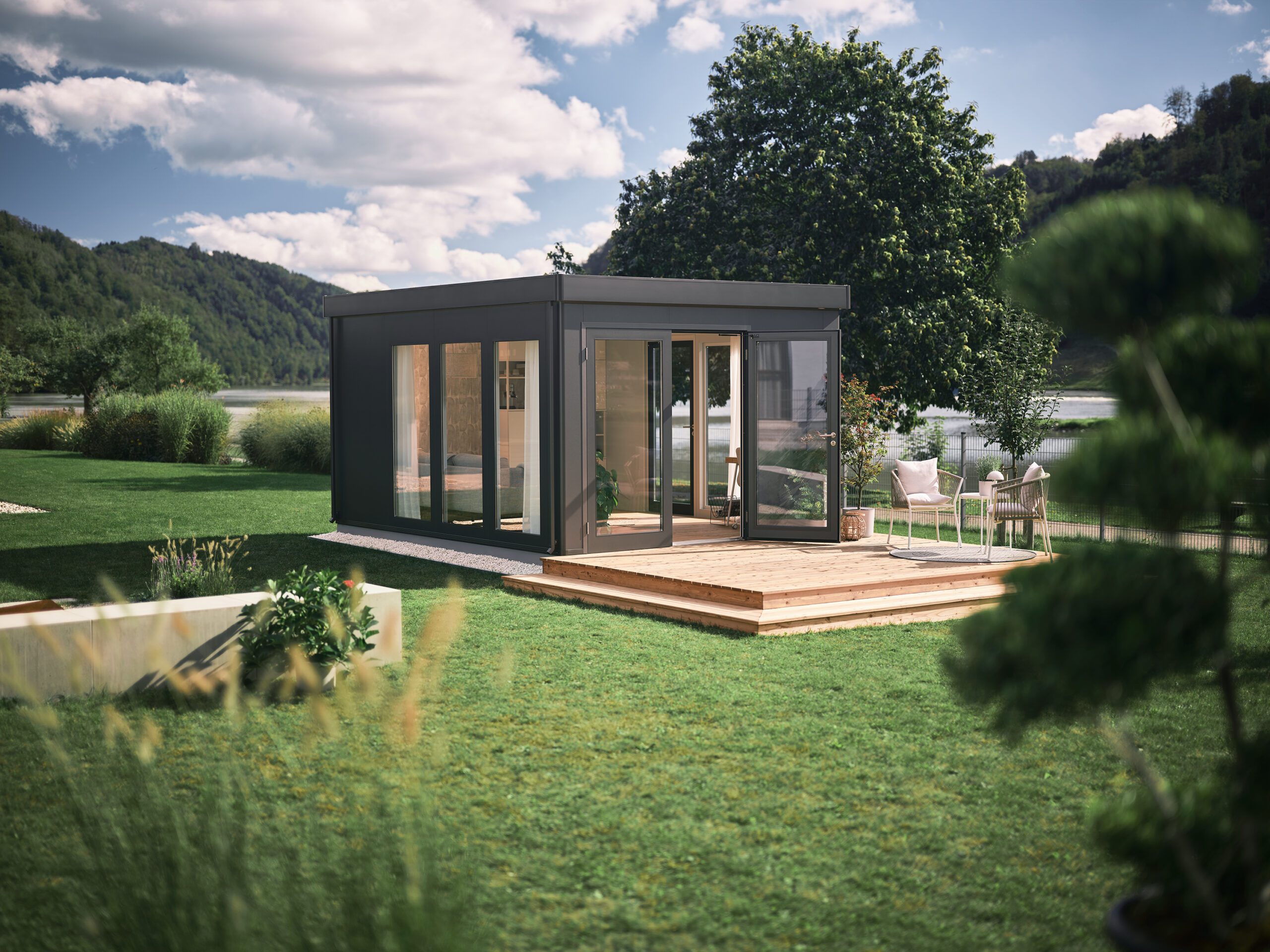 Dunkelgraues, modernes Gartenhaus und erweiterter Wohnraum mit Ganzglastüren, Fenstern und Flachdach in einem grossen Garten. Erweiterter Wohnraum kaufen Schweiz.