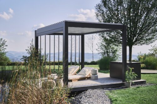 Dunkelgraue, freistehende Pergola mit verstellbaren Dach- und Seitenlamellen in einem grossen Garten.