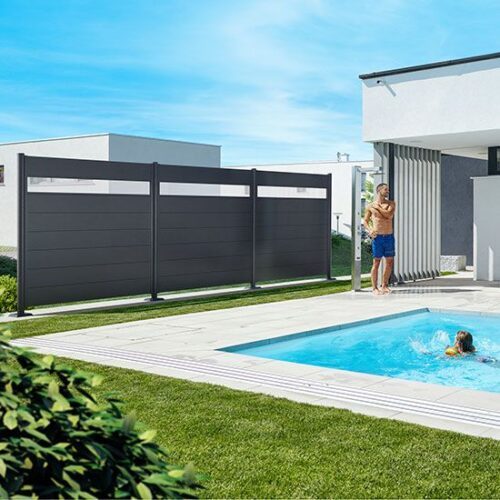 Brise-vue Biohort en gris foncé métallique avec une partie supérieure en verre acrylique. Le brise-vue est installé dans un jardin devant une piscine.