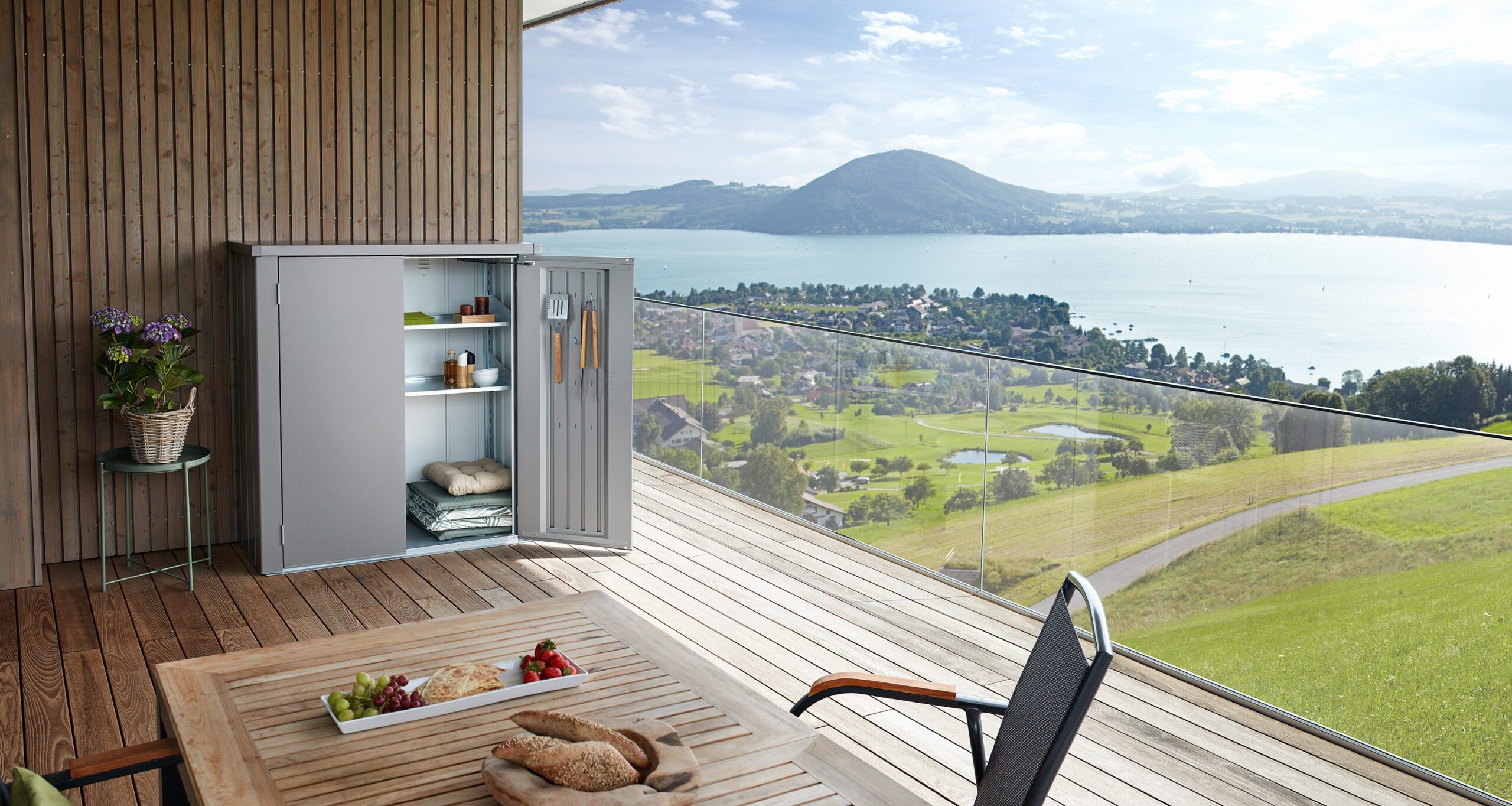 Terrassenbox Balkonbox auf Holzterrasse mit Ausblick auf einen See.