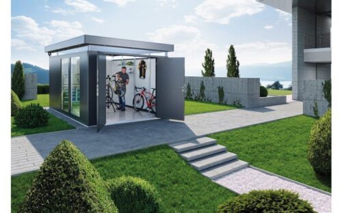Grosses Metallgartenhaus mit grossen Fensterelementen an den Seiten. Steht in einem Garten vor einem grossen Haus.