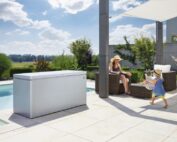 Terrasse mit Pool, Biohort Gartenbox in silber und Gartenlounge. Eine Frau mit Sonnenhut sitzt in der Gartenlounge.
